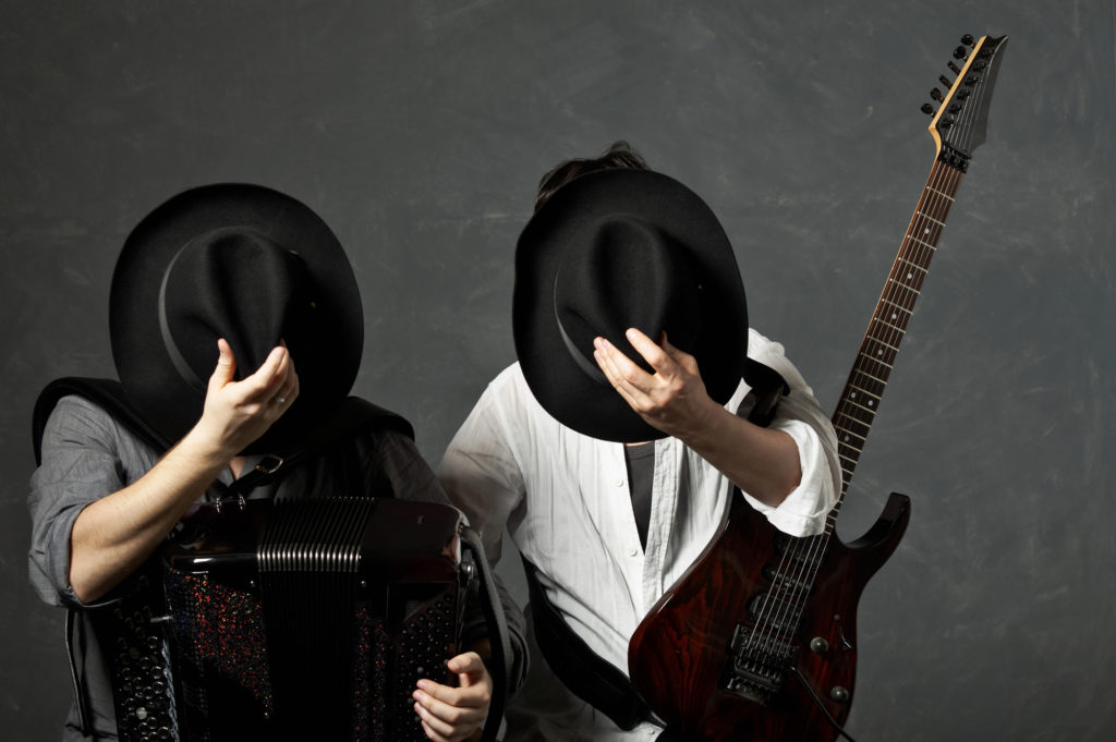 Two musicians with a guitar and an accordion close the face hats